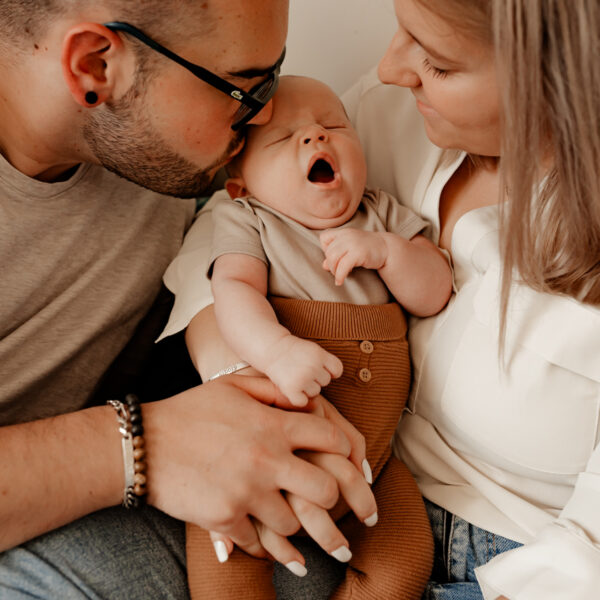 portrait de famille d'un couple embrassant leur bébé qui est entre eux en train de bailler