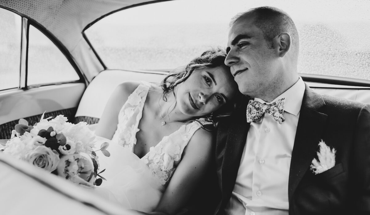 Portrait des mariés à l'arrière de leur voiture le jour de leur mariage