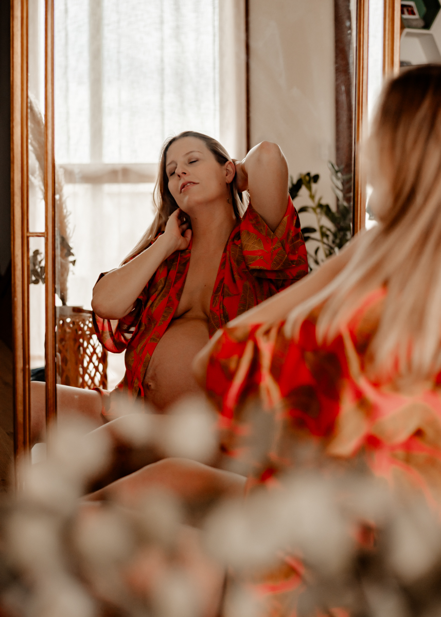 Femme enceinte devant son miroir pendant sa séance photo de grossesse à domicile