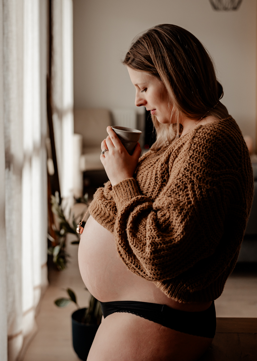 Femme enceinte buvant son thé chez elle pendant sa séance photo de grossesse à domicile